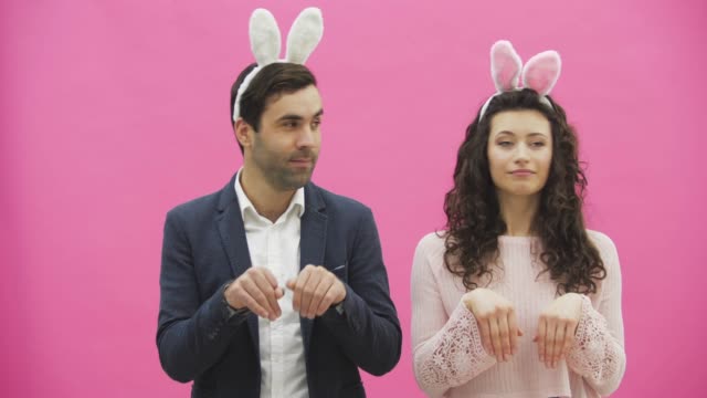 Young-couple-standing-standing-on-pink-background.-During-this-time,-they-are-dressed-in-rabble-ears.-Looking-gently-at-each-other,-rhythmically-simultaneously-turning-his-head-to-the-side.-Easter.