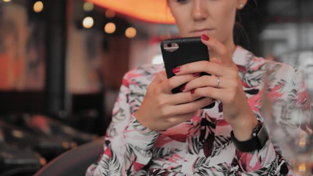 Unrecognized-young-female-French-woman-uses-a-smartphone-while-sitting-in-a-restaurant.-On-the-hand-is-a-smart-watch.-Slow-Motion