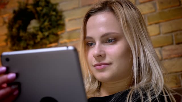 Closeup-portrait-of-young-woman-with-blonde-hair-using-the-tablet-indoors-at-cozy-home