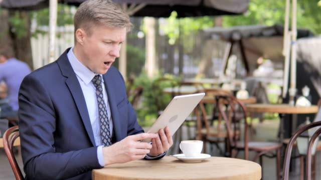 Businessman-Upset-by-Loss-on-Tablet,-Sitting-in-Outdoor-Cafe