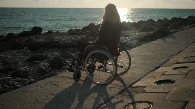 Junge-Dame-mit-Wirbelsäulenerkrankung-sitzt-im-Rollstuhl-an-der-Küste-des-Meeres