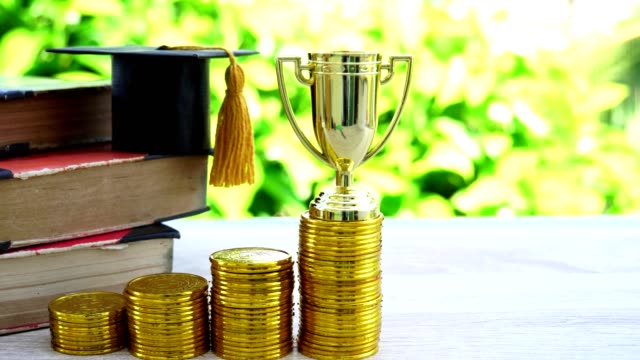 Gestión-del-campeón-de-logros-con-la-inversión-de-premios-en-concepto-financiero:-trofeo-de-oro-en-las-primeras-filas-de-monedas-de-oro,-sombrero-de-graduación,-caja-de-lápices,-libro-de-texto-antiguo.-El-éxito-en-la-vida-de-la-educación-empresarial