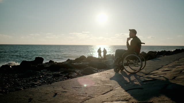 Solitario-adulto-discapacitado-hombre-está-contemplando-la-vista-al-mar,-sentado-en-la-orilla-del-mar