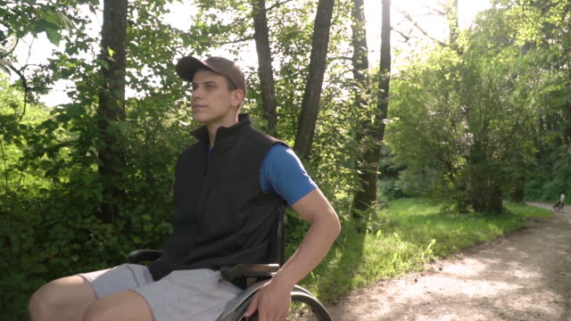 Slowmotion-Frontgesicht-folgen-von-behinderten-jungen-Studenten-Mann-in-einem-Rollstuhl-beobachten-die-Natur-um-ihn-herum,-mit-Sonnenbrand