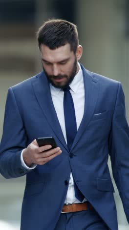 Successful-Business-Man-Uses-Smartphone-While-Walking-on-the-Big-City-Business-District-Street.-Video-Footage-with-Vertical-Screen-Orientation-9:16