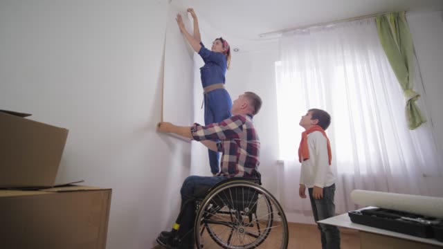 Geliebte-behinderte-im-Rollstuhl-glücklich-Person-wählt-junge-schöne-Frau-neue-Tapete-im-Zimmer-während-der-Reparatur