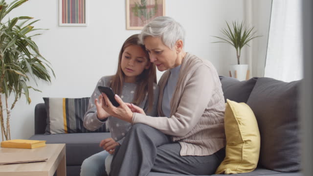 Teenage-Girl-Helping-Grandmother-Mastering-Phone