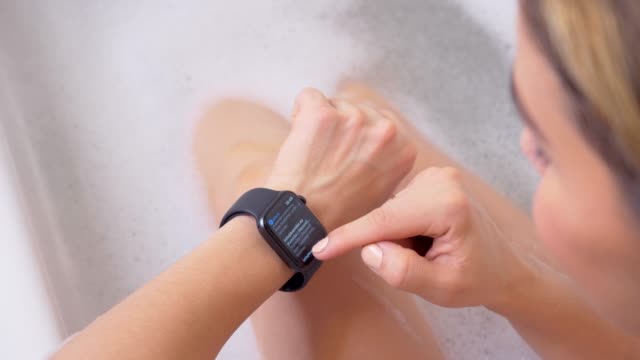 Attractive-young-woman-athlete-wearing-and-using-smartwatch-in-bathroom.-Taping-smartwatch-device-screen.