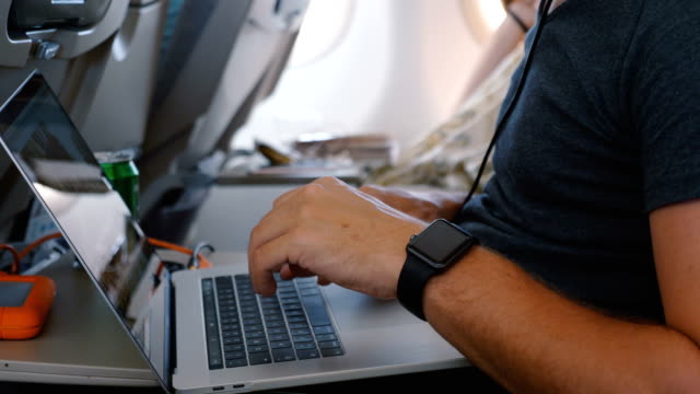 Close-up-young-freelance-businessman-with-smart-watch-using-laptop-to-work-online-during-airplane-business-trip-flight.