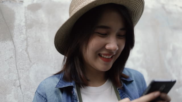 Lächelnd-von-asiatischen-Frau-trägt-Retro-Fedora-Hut-mit-Smartphone-Typisierung-Nachricht,-Surfen-Social-Media-Sharing-Reise-mit-ihren-Freunden-im-Urlaub-Sommer.