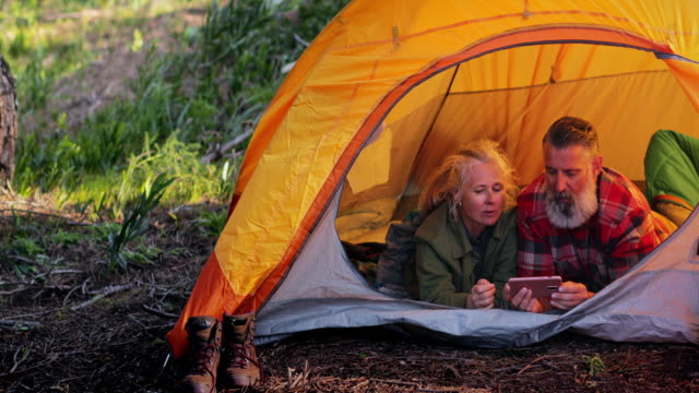 Close-up-senior-couple-using-smartphone-inside-tent-in-forest