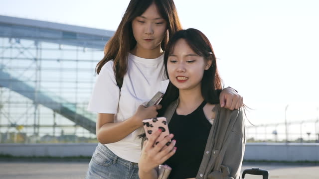 Schöne-25-Jahre-alte-asiatische-Mädchen-mit-langen-Haaren-suchen-in-Telefon-und-lächelnd-in-der-Nähe-des-modernen-Flughafengebäude