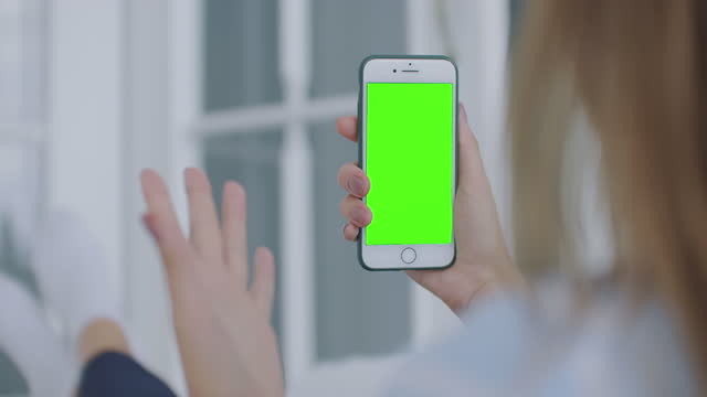 Woman-using-for-video-call-mobile-phone-vertical-green-screen.-Female-holding-in-hand-portable-gadget-close-up-indoors-home-living-room.-Mock-up-for-tracking-or-watching-content.