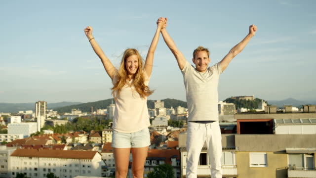 CLOSE-UP:-Happy-brother-and-sister-standing-on-rooftop-raising-hands-in-the-sky