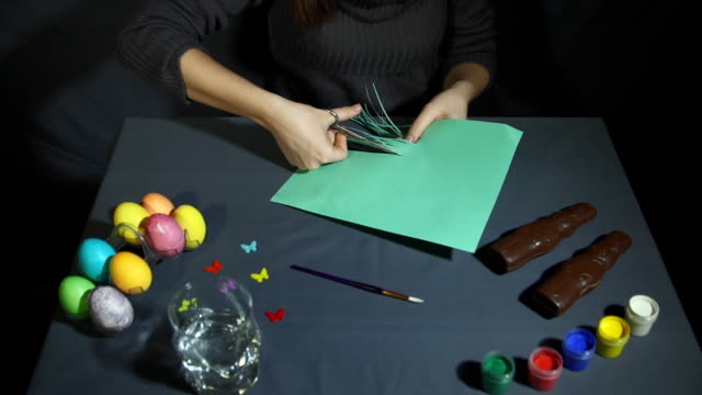 Weibliche-Hände-in-dünne-Fransen-geschnitten-das-Grünbuch-mit-einer-Schere-über-graue-Tisch.