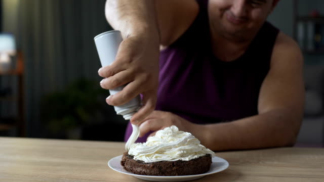 Fat-male-decorating-cake-with-whipped-cream-and-putting-cherry-on-the-top