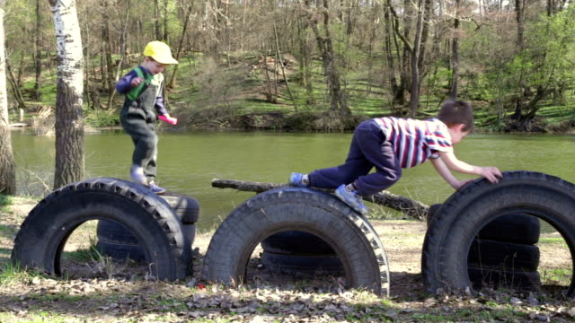 Two-kids-playing-together,-jumping-and-climbing-on-tires