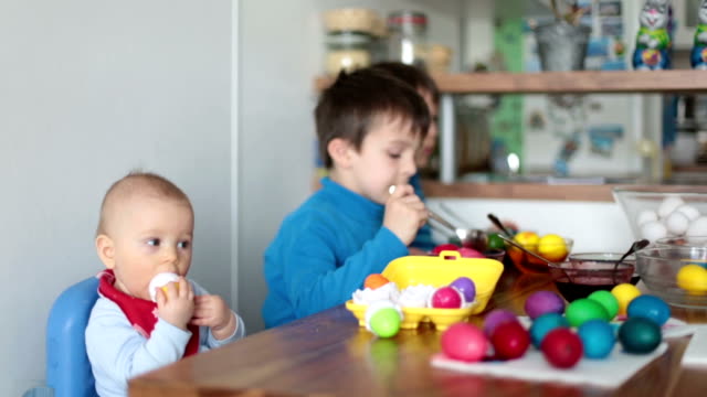 Three-children,-brothers,-coloring-and-painting-easter-eggs-at-home-in-kitchen-for-the-holiday