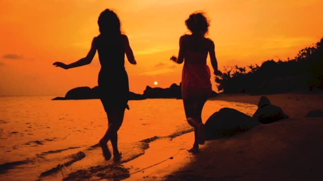 two-happy-girls-running-into-water-at-sunset-in-slow-motion
