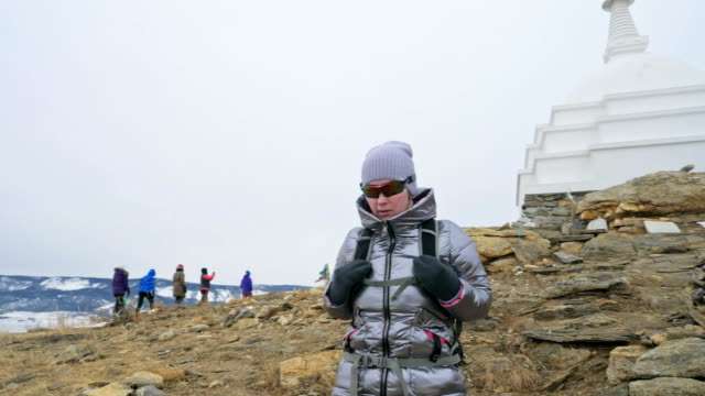 Travel-of-woman-on-ice-of-Lake-Baikal.-Close-unique-buddhist-stupa-burkhan-monument-symbol-mystical-historic-ritual-island-Ogoi-landscape-mountains-shamanic-worship.-Trip-to-winter-island.