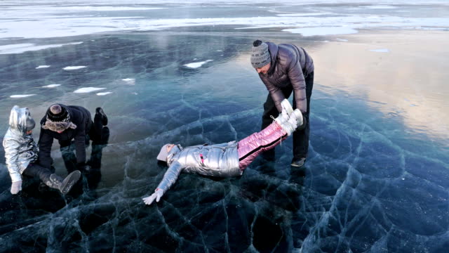 Family-is-having-fun-on-beautiful-ice-in-cracks.-Father-mother-son-and-daughter-funny-fight-on-ice,-make-sandwich-and-rest.-Man,-woman-and-children-are-resting-on-lake-of-Baikal.