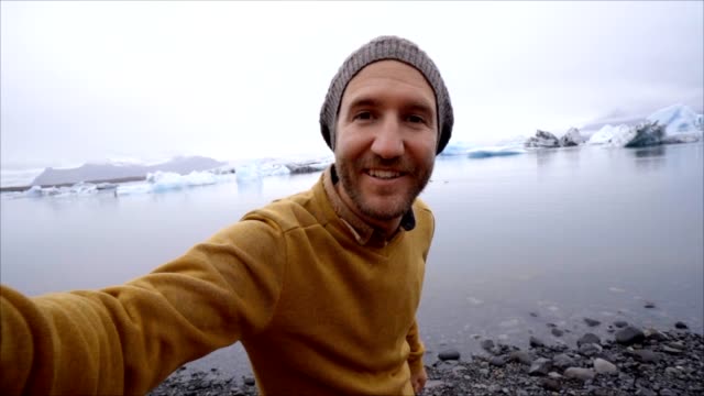 Young-man-taking-selfie-with-glacier-lake,-icebergs-floating-on-water-in-Iceland