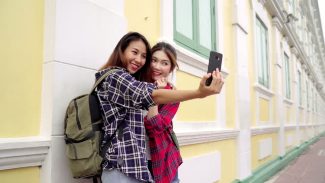 Viajero-mochilero-mujeres-asiáticas-lesbianas-lgbt-par-de-viajes-en-Bangkok,-Tailandia.-Bloguero-feliz-joven-pareja-mujer-con-smartphone-para-selfie.
