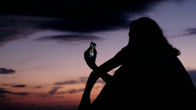 Silhouette-eines-Mädchens-nutzt-eine-Smartphone,-auf-soziale-Netzwerke-bei-Sonnenuntergang-zu-leben