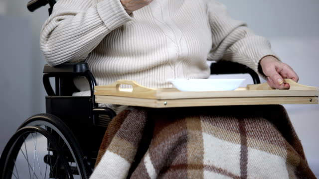 Lonely-elderly-woman-in-wheelchair-eating-dinner-and-crying,-health-problems