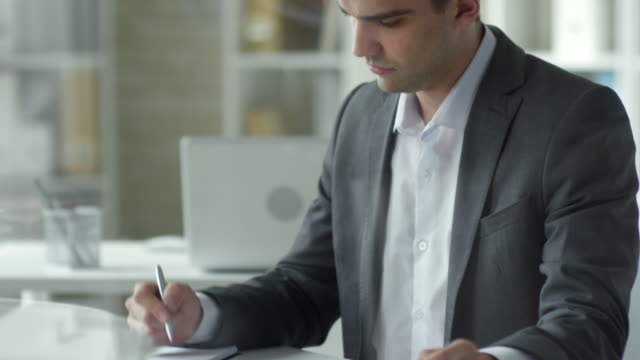 Hombre-de-negocios-caucásico-usando-Tablet-y-tomando-notas-en-Office-Desk