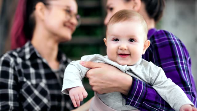 Portrait-of-sweet-little-baby-posing-looking-at-camera-female-couple-in-background