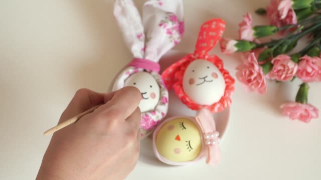 El-cierre-de-la-mano-femenina-con-brocha-dibuja-huevos-de-Pascua-de-pollo-decorados-para-liebres-de-Pascua-y-pollos