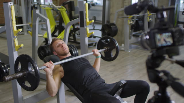 Male-Trainer-Showing-Barbell-Press-on-Camera