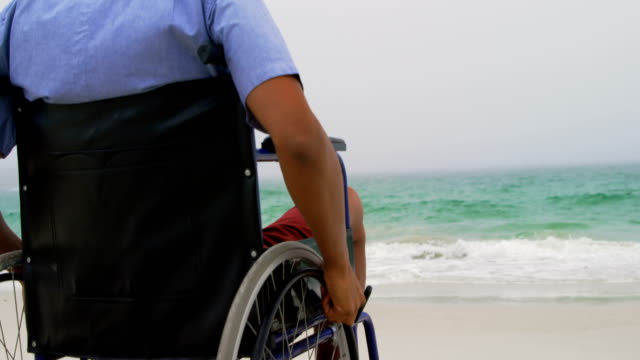 Vista-trasera-del-hombre-afroamericano-sentado-en-silla-de-ruedas-en-la-playa-4k