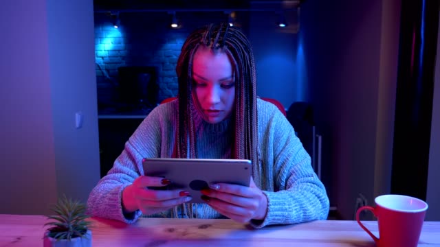 Closeup-shoot-of-young-attractive-female-blogger-with-dreadlocks-playing-video-gameson-the-tablet-losing-and-being-frustrated-streaming-live-with-the-neon-background-indoors