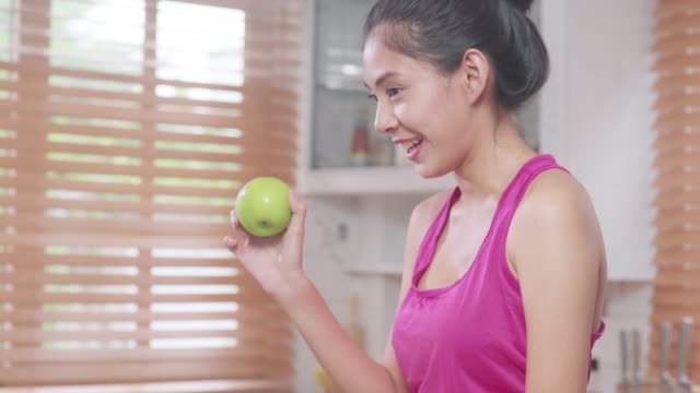Asian-blogger-woman-make-vlog-how-to-diet-and-lost-weight,-Young-female-using-camera-recording-when-she-eating-fruits-in-the-kitchen.-Lifestyle-influencer-women-healthy-concept.