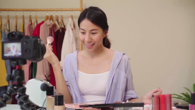 Slow-motion---Beauty-blogger-present-beauty-cosmetics-sitting-in-front-camera-for-recording-video.-Happy-beautiful-young-Asian-woman-use-cosmetics-review-make-up-tutorial-broadcast-live-video.