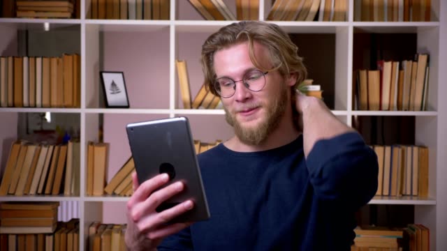 Nahaufnahme-von-erwachsenen-attraktiven-männlichen-Studenten-mit-einem-Videoanruf-auf-dem-Tablet-in-der-Universitätsbibliothek-drinnen
