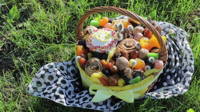 Metraje-de-cesta-con-pastel-de-Pascua,-frutos-secos-y-frutos-secos-en-la-hierba-verde-en-el-jardín