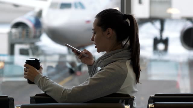 Mädchen-mit-Takeaway-Kaffee-in-der-Hand-zeichnet-Sprachnachricht-am-Telefon-am-Flughafen