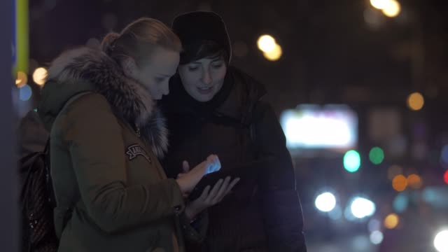 Mujeres-amigas-que-utilizan-tablet-PC-cuando-esperan-el-autobús-en-la-calle