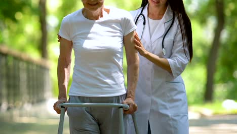 Female-doctor-helping-to-mature-lady-moving-with-walking-frame,-physiotherapy