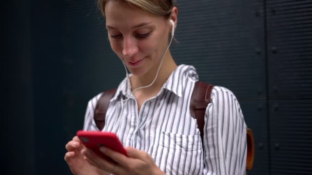 Efecto-de-cámara-lenta-de-la-mujer-feliz-escuchando-música-en-auriculares-y-escribiendo-sms-de-texto-a-través-de-la-aplicación-móvil