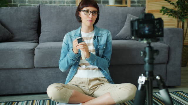 Blogger-mujer-grabando-vídeo-sobre-el-reloj-digital-usando-la-cámara-en-apartamento