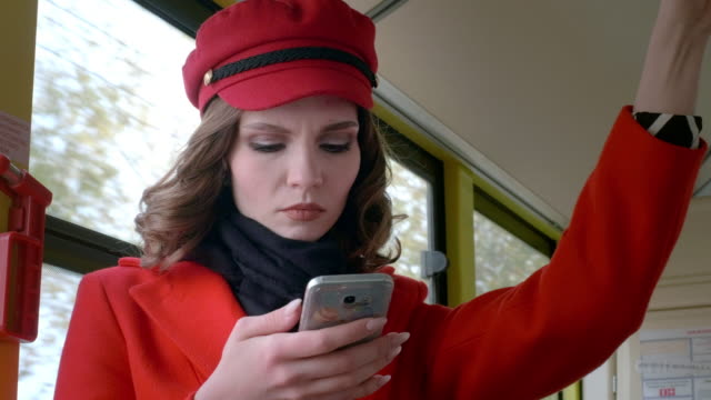 Porträt-eines-eleganten-jungen-Mädchens-in-einem-roten-Mantel.-Verwendet-ein-Smartphone-in-öffentlichen-Verkehrsmitteln.-Druckt-eine-Textnachricht-im-Bus