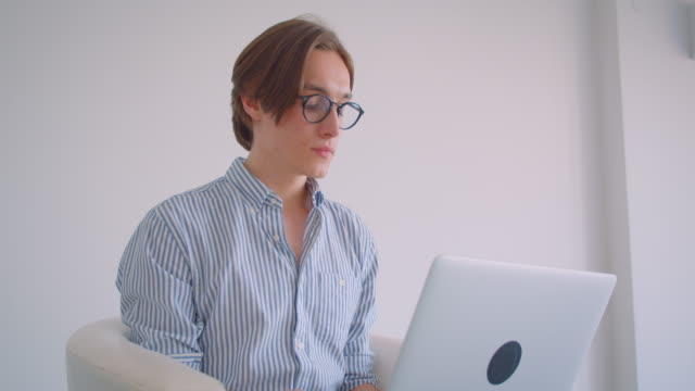 Retrato-de-primer-plano-de-joven-atractivo-empresario-caucásico-trabajando-en-el-ordenador-portátil-sentado-en-el-sillón-interior