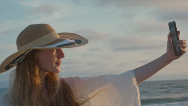 Mujer-joven-tomando-un-selfie-junto-al-océano-durante-la-puesta-del-sol