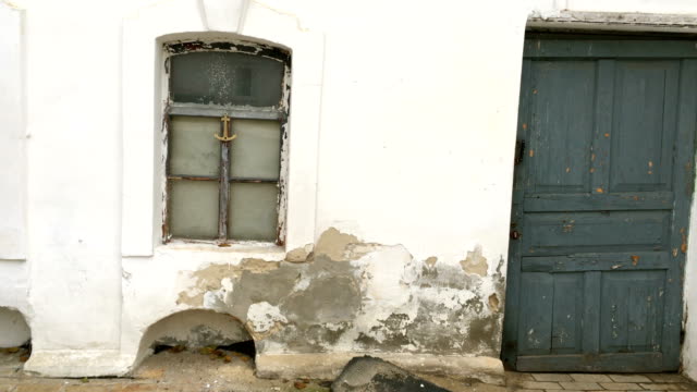 Weathered-and-damaged-wall-of-old-house,-plaster-white-with-damage-and-cracks.