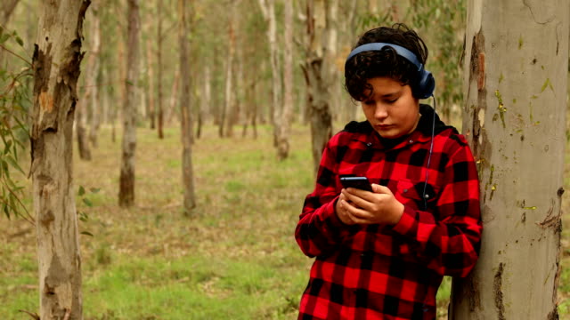 Adolescente-niño-con-auriculares-usando-teléfono-inteligente-en-la-naturaleza