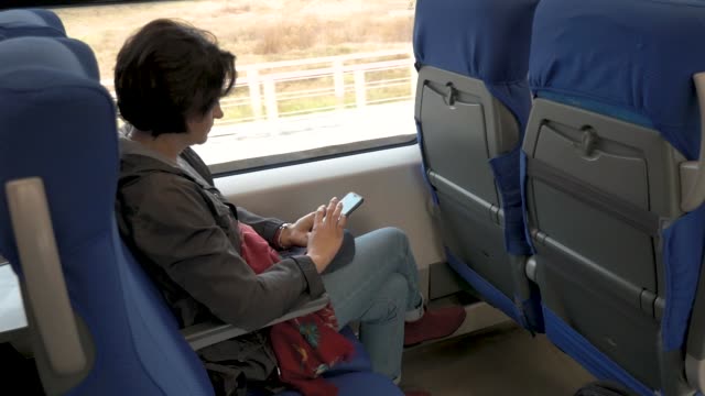 mujer-está-sentada-en-el-tren-sosteniendo-el-teléfono-celular-en-sus-manos-Haciendo-clic-en-la-vista-lateral-trasera